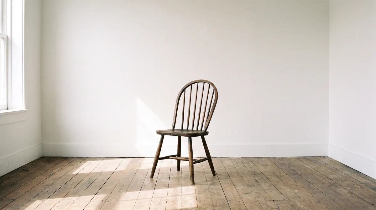 A finished bow-back Windsor chair standing alone in a white room with a bare wooden floor.